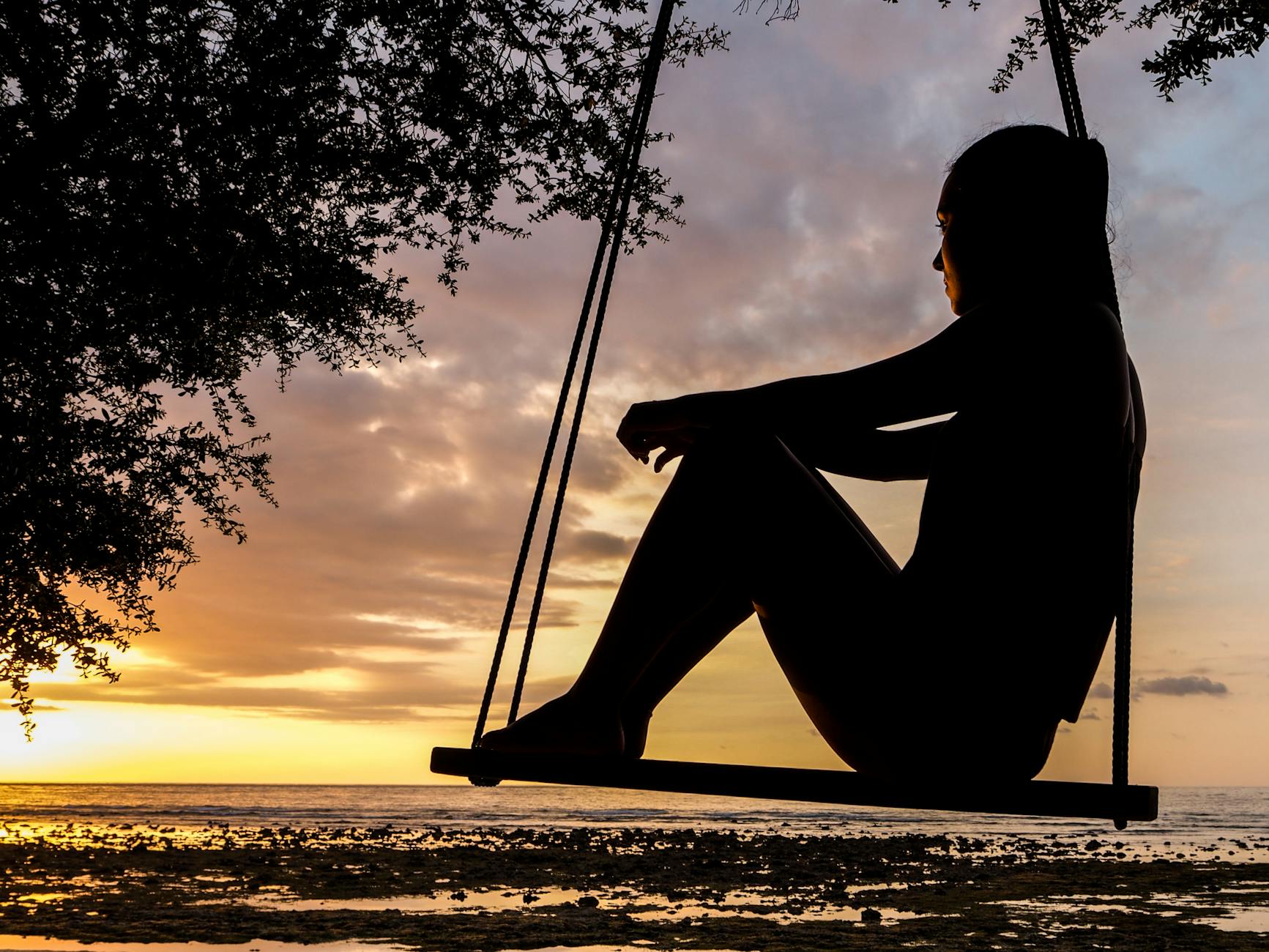 silhouette of woman on swing during golden hour